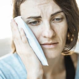 Woman holding an ice pack up to her ear.