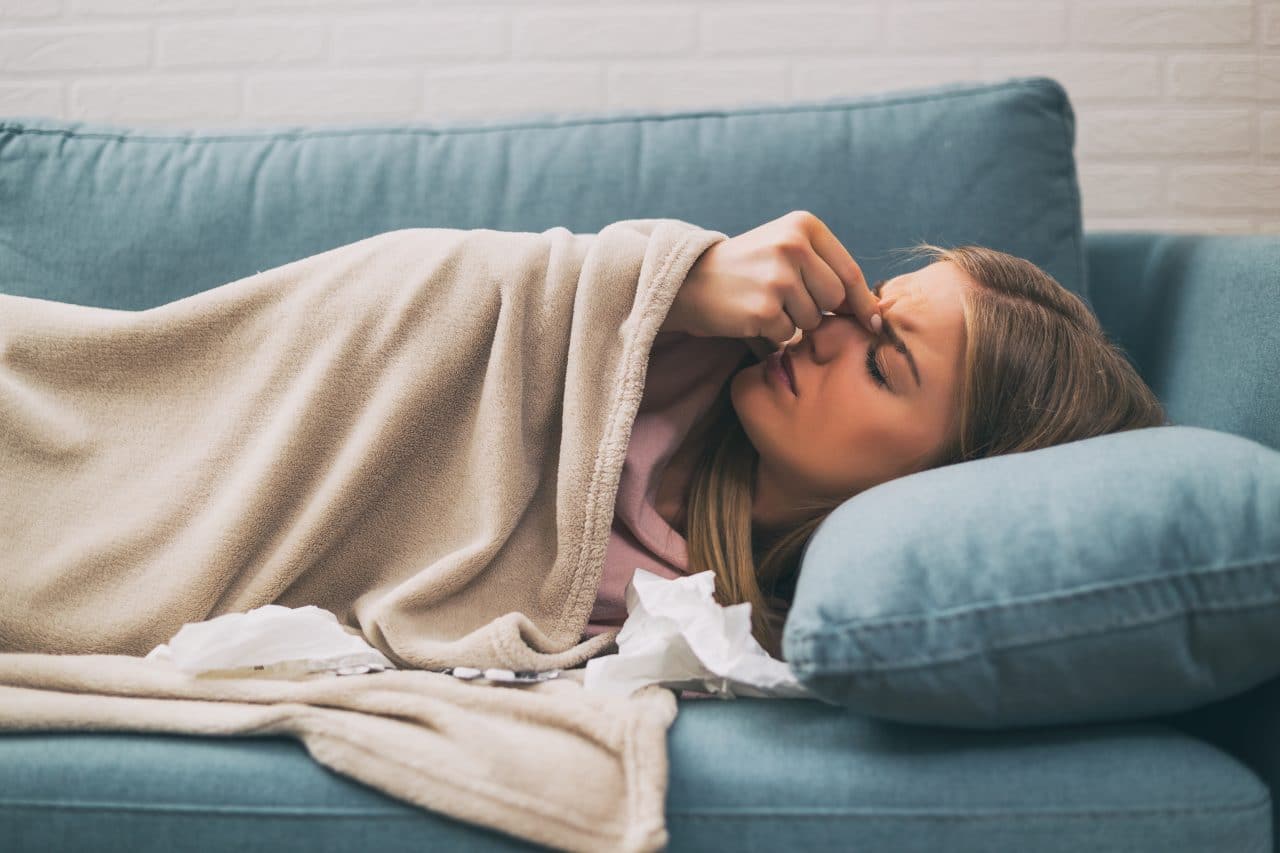 Woman experiencing allergy symptoms while lying on couch.