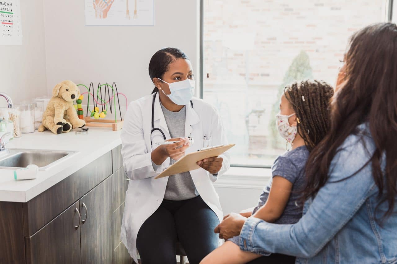 With a protective mask on, a female pediatrician talks to a young patient's mother about the woman's daughter's medical conditions. They are wearing protective masks.