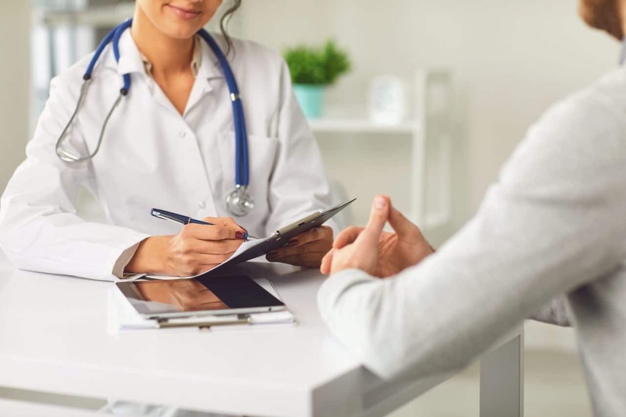 A doctor sitting down and speaking with her patient in a clinical setting.