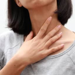 Closeup of woman touching her sore throat.
