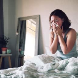 Woman blowing her nose while sick in bed.