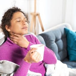 Woman suffering with a sore throat at home.
