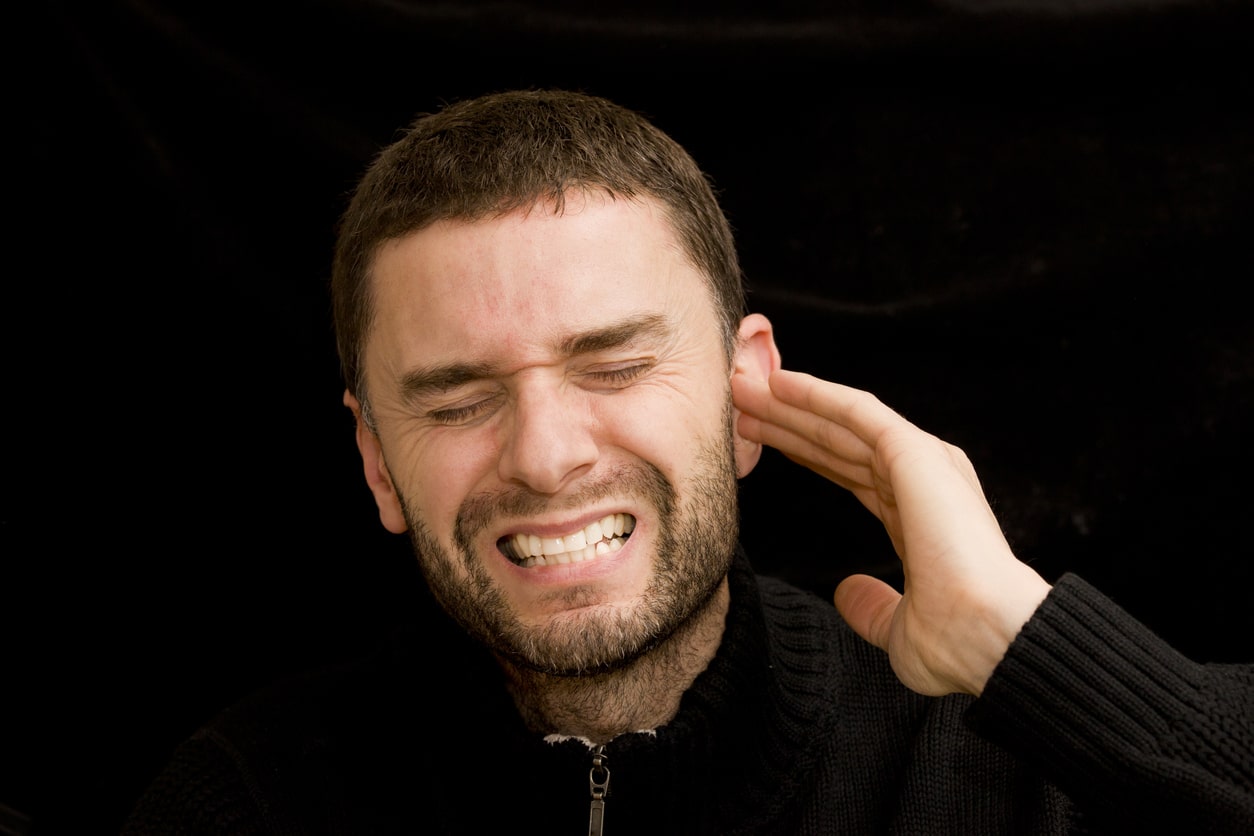 man in sweater holding ear in visible pain