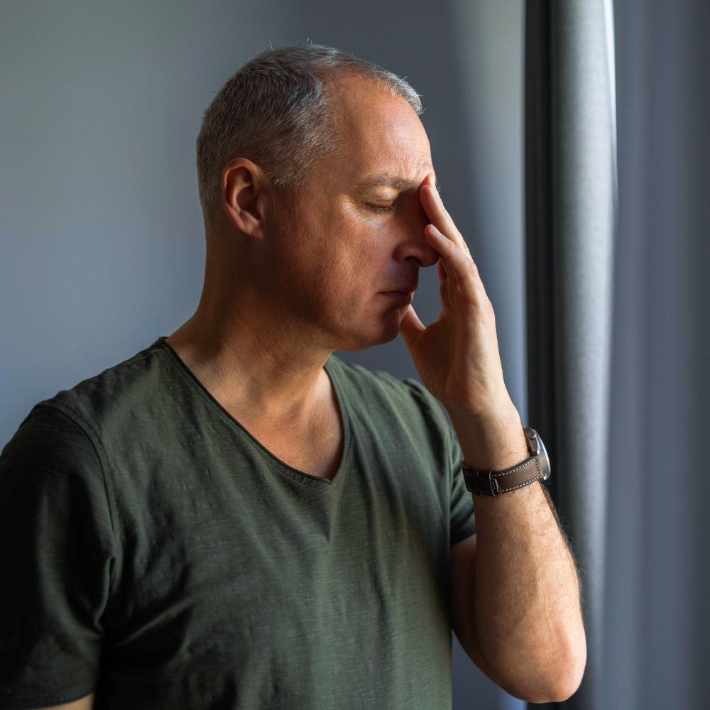 a man stands indoors with his hand on his nose in discomfort