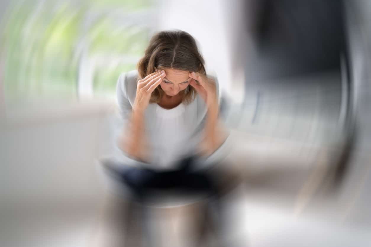 Woman with vertigo sitting down and holding her head.