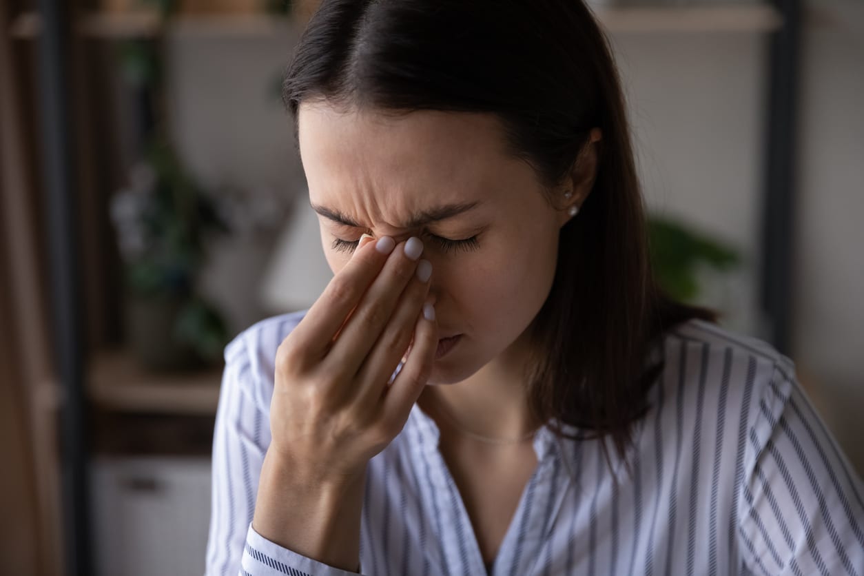 Woman with sinus pressure holding the bridge of her nose.