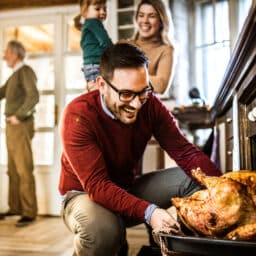 Man taking a Thanksgiving turkey out of the oven surrounded by his family