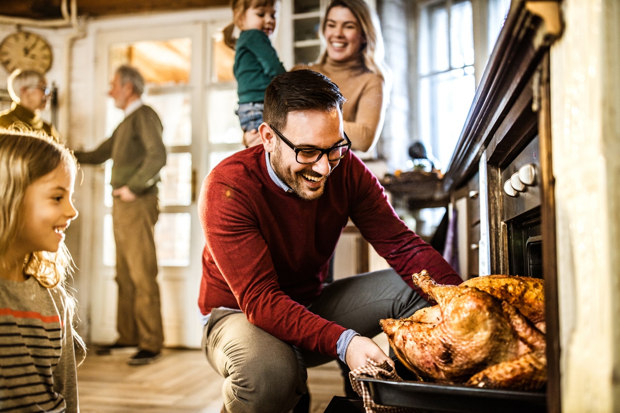 Man taking a Thanksgiving turkey out of the oven surrounded by his family.