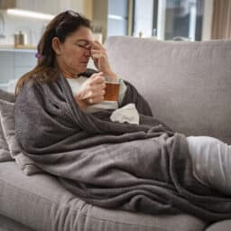 Sick woman resting on sofa drinking hot tea and massaging her nose