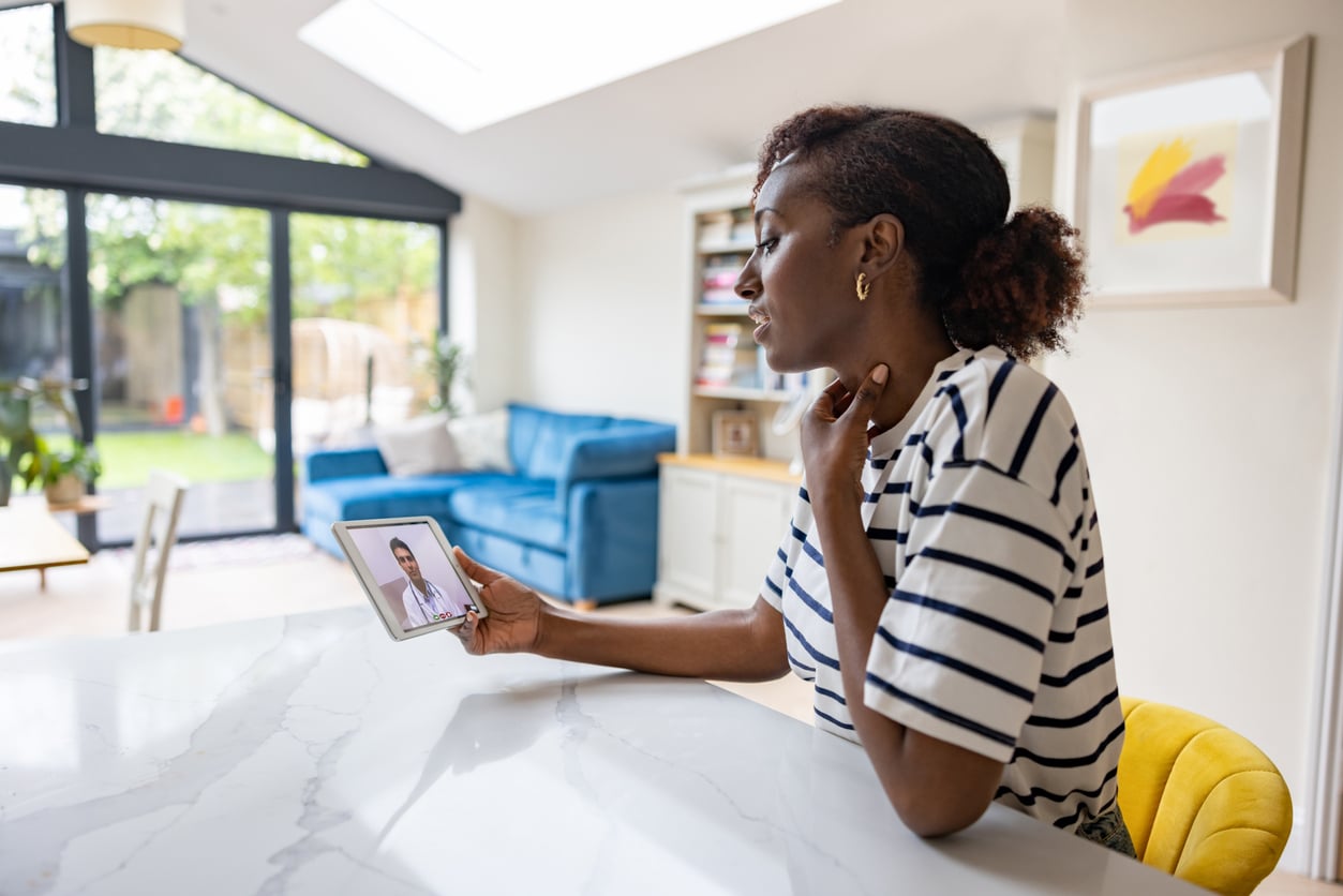 Woman at home talking to a doctor about her sore throat on a video call.