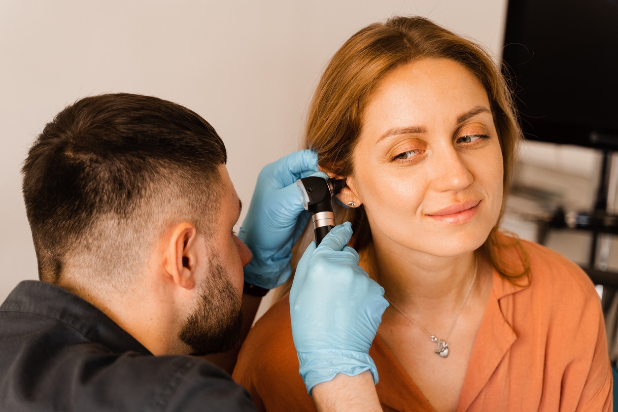 Otolaryngologist looks through otoscope the ears of woman.