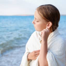 Young girl at the beach tugging on her ear, trying to get water out