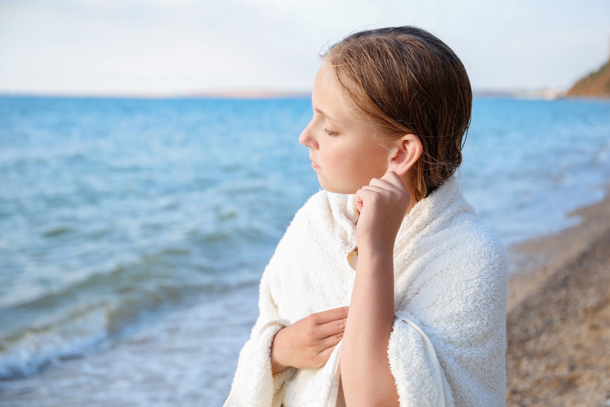 Young girl at the beach tugging on her ear, trying to get water out.