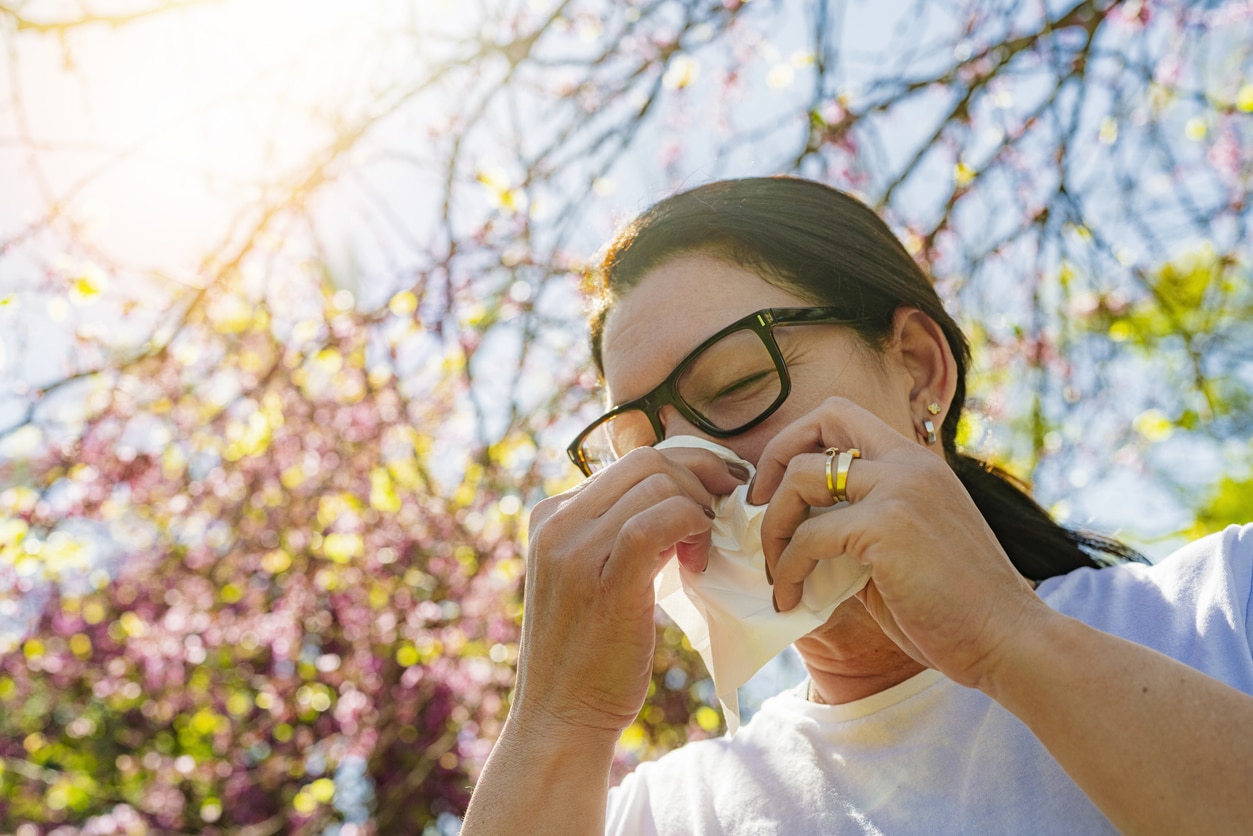 Woman with seasonal allergy using paper tissue to blow her nose.